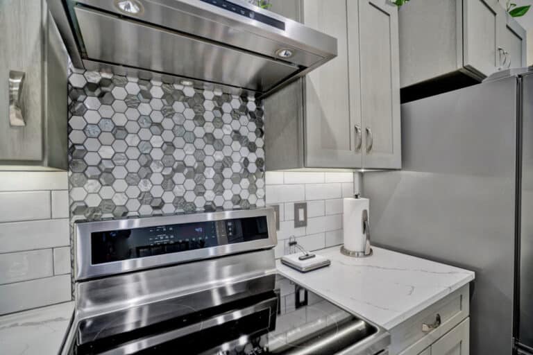 Gray shaker cabinets, with white countertop, and patterned backsplash on stove