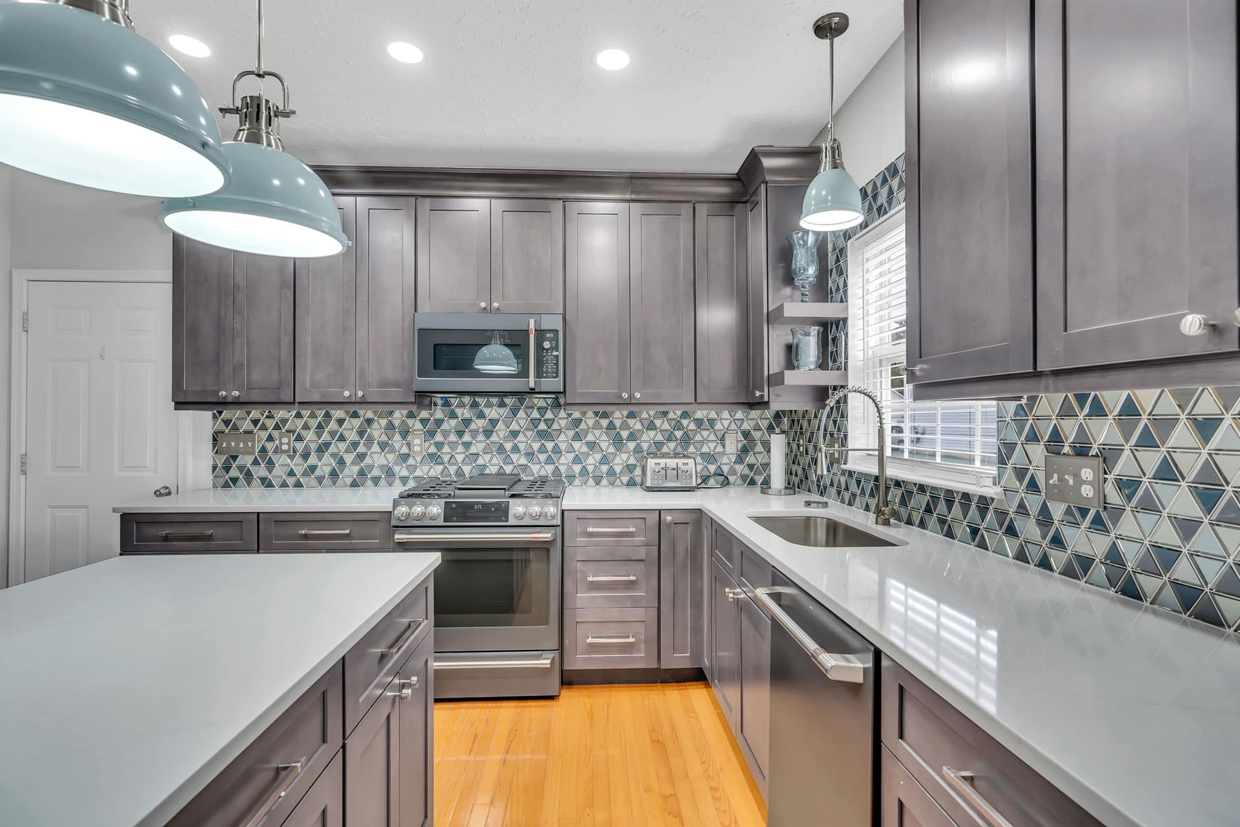 Spacious kitchen project in waldorf md with gray shaker cabinets, white countertop, patterned backsplash, and wood flooring