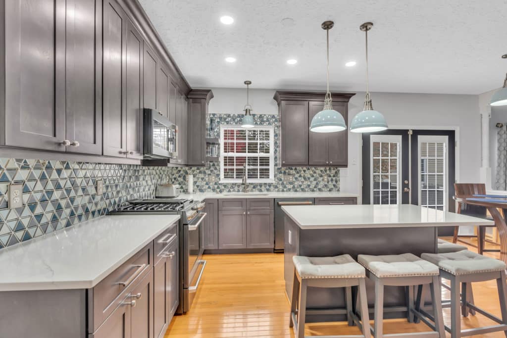 Spacious kitchen project in waldorf md with gray shaker cabinets, white countertop, patterned backsplash, and wood flooring