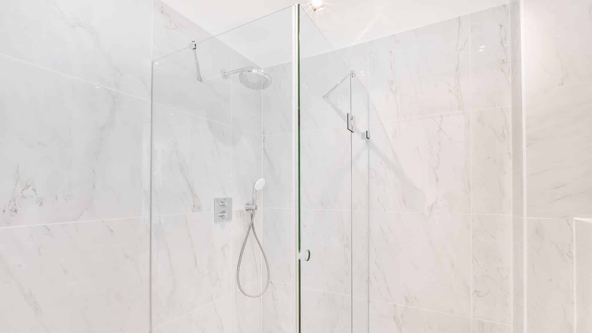 Glass enclosed shower on white tiles surround